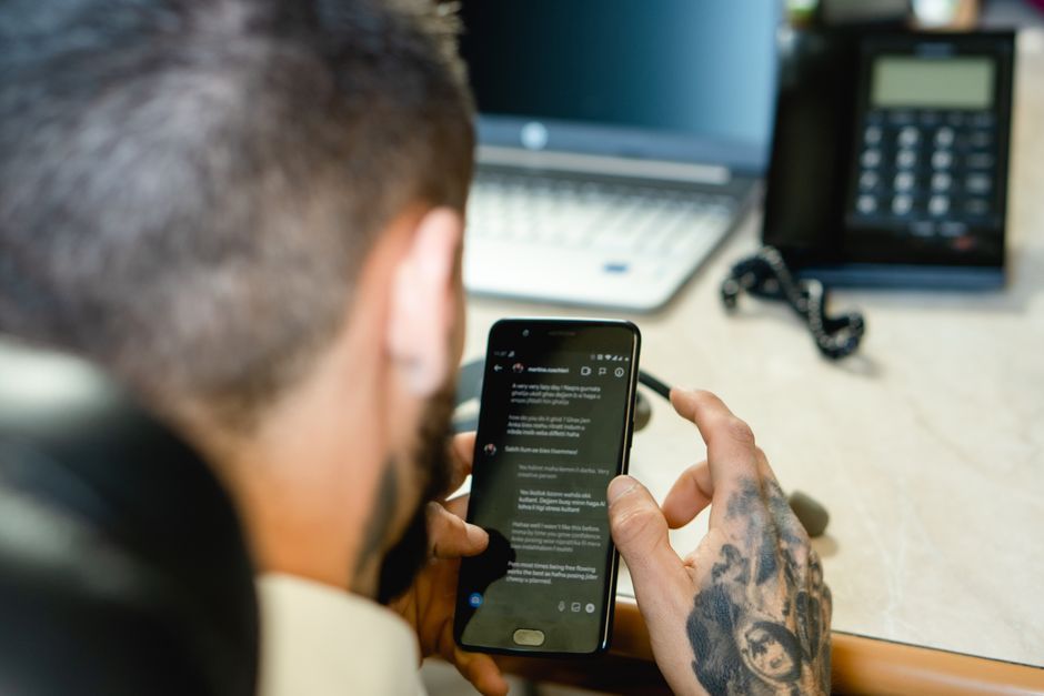 person using smartphone messaging laptop workspace