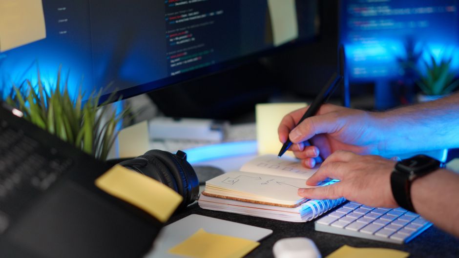 software developer writing code notebook computer office desk workspace